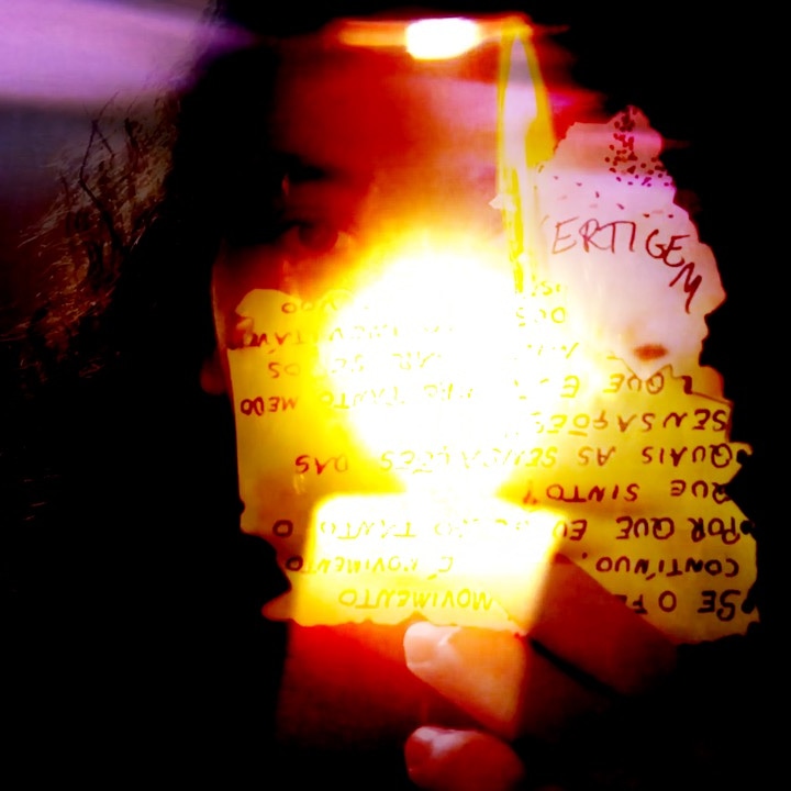 Imagem colorida em sobreposição. Ao fundo, um rosto feminino e uma mão diante dele, segurand uma vela. à frente, uma carta com escritos diversos. 